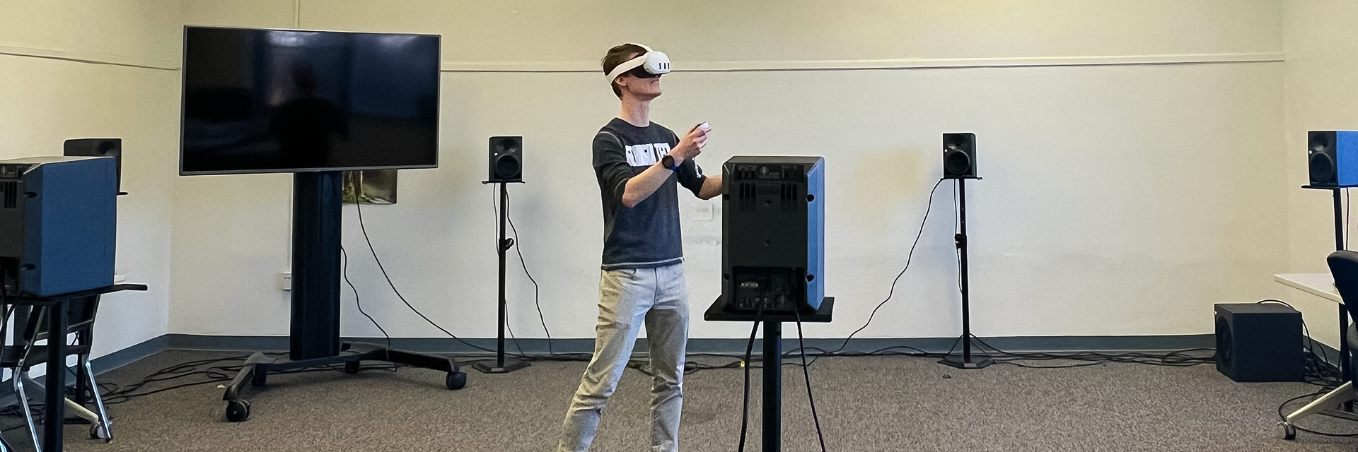 A student wears a virtual reality headset while working with a series of speakers.